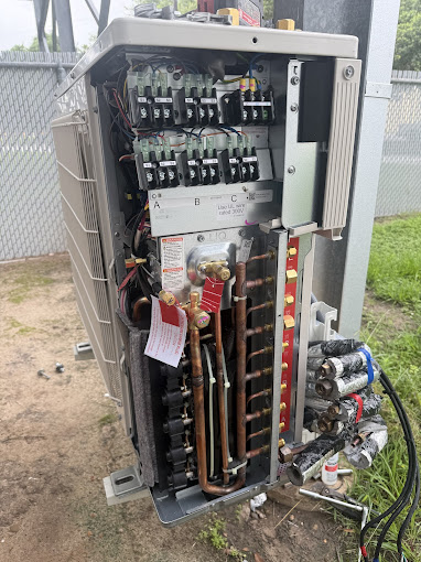 Texas Heatwave technician servicing an opened heat pump outdoor unit with copper refrigerant lines and controls exposed